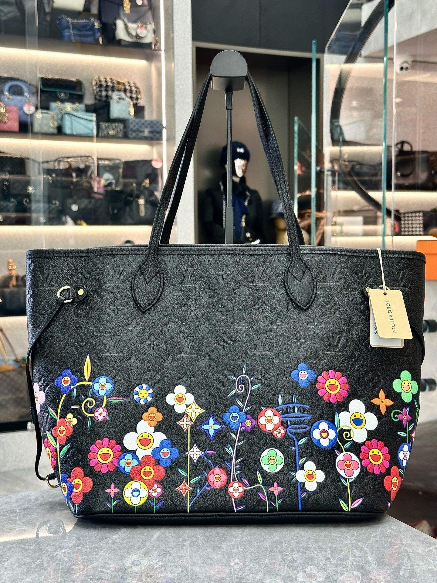 Louis Vuitton x Takashi Murakami Neverfull MM is crafted from black Monogram Empreinte leather and features a vibrant, multicolored floral print