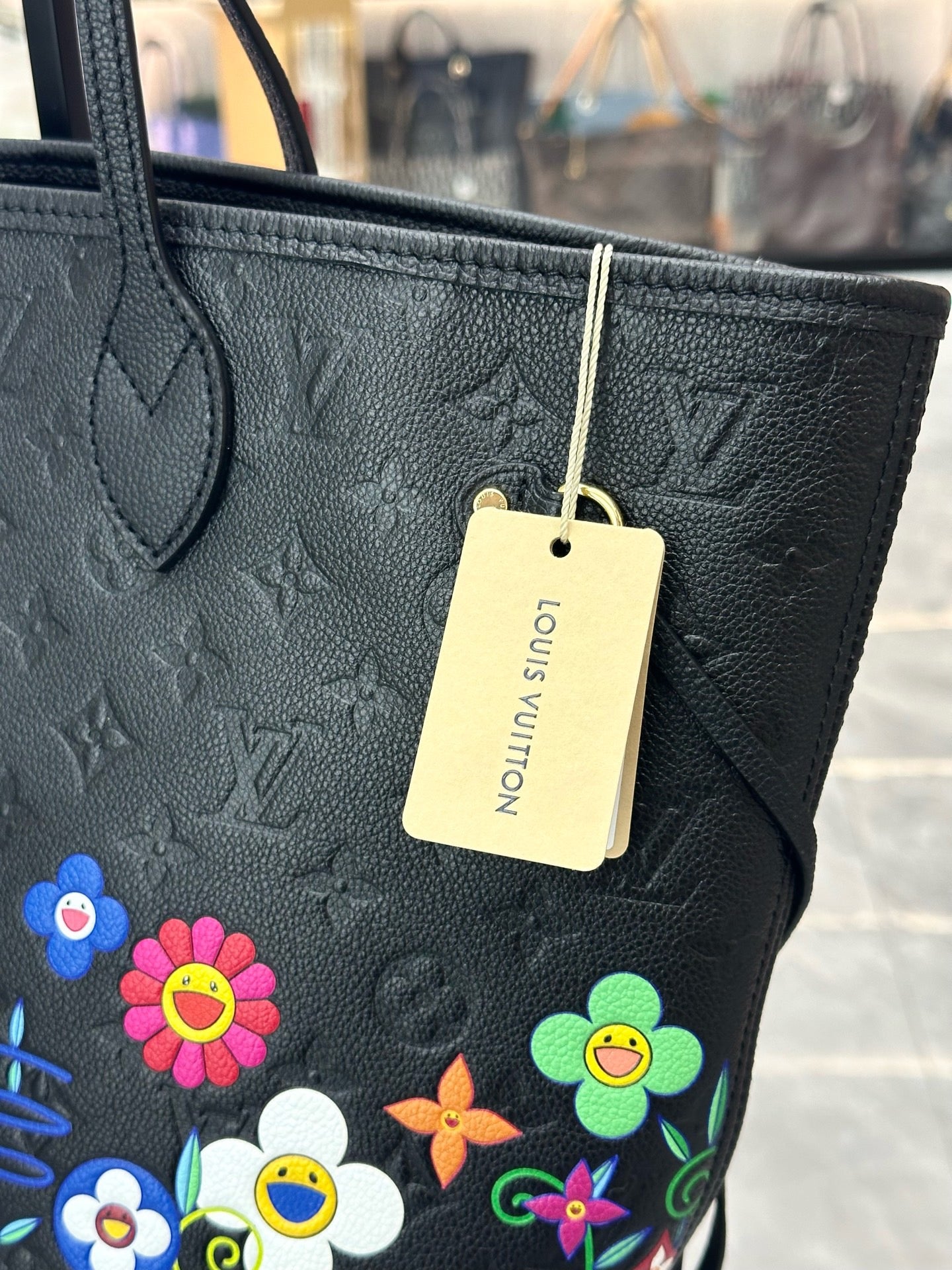Louis Vuitton x Takashi Murakami Neverfull MM is crafted from black Monogram Empreinte leather and features a vibrant, multicolored floral print