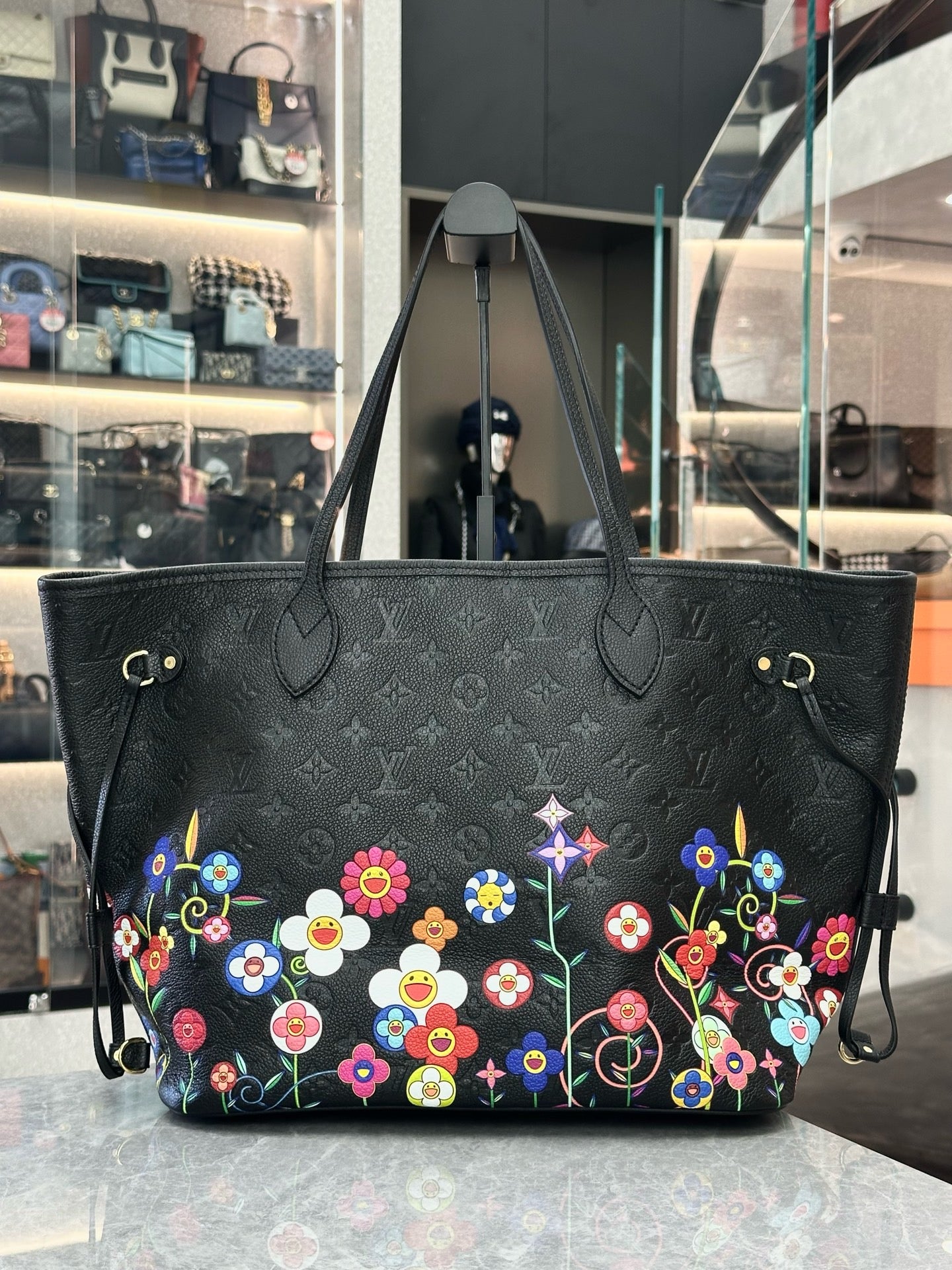 Louis Vuitton x Takashi Murakami Neverfull MM is crafted from black Monogram Empreinte leather and features a vibrant, multicolored floral print