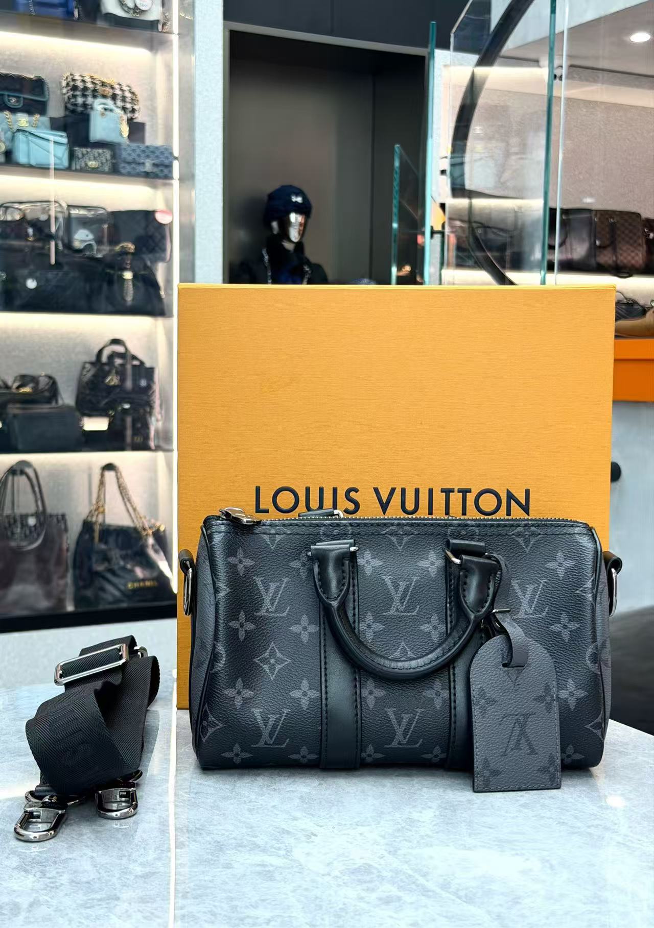 Louis Vuitton Keepall Bandoulière 25 in Monogram Eclipse canvas features black leather trim and silver-tone hardware