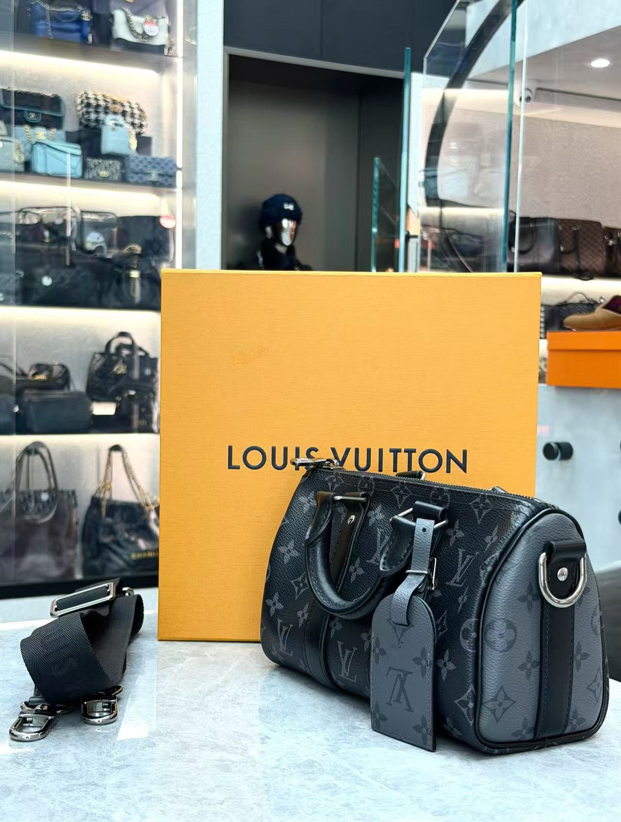 Louis Vuitton Keepall Bandoulière 25 in Monogram Eclipse canvas features black leather trim and silver-tone hardware