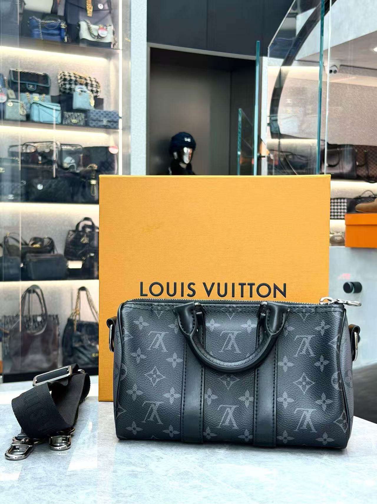 Louis Vuitton Keepall Bandoulière 25 in Monogram Eclipse canvas features black leather trim and silver-tone hardware
