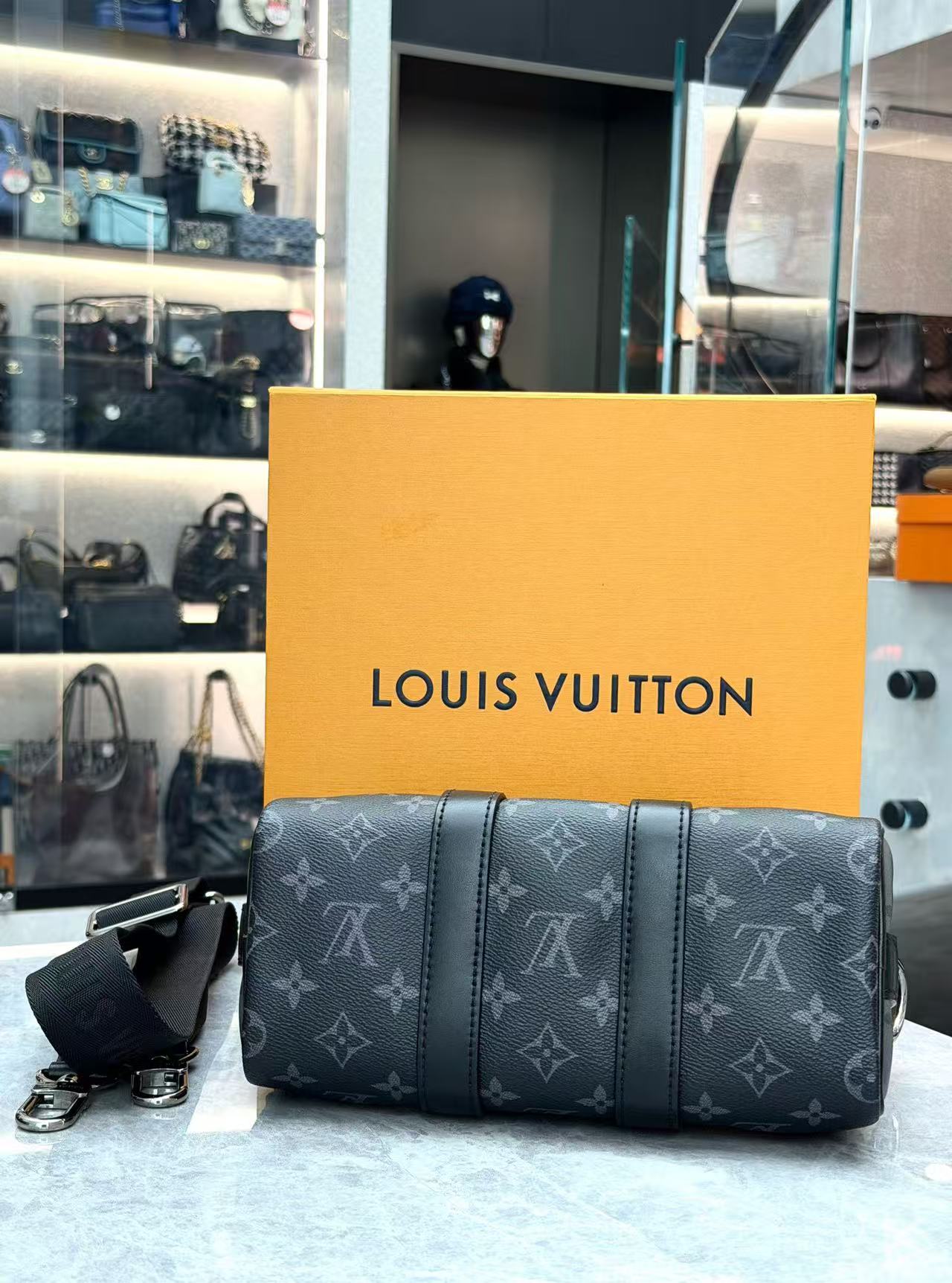 Louis Vuitton Keepall Bandoulière 25 in Monogram Eclipse canvas features black leather trim and silver-tone hardware