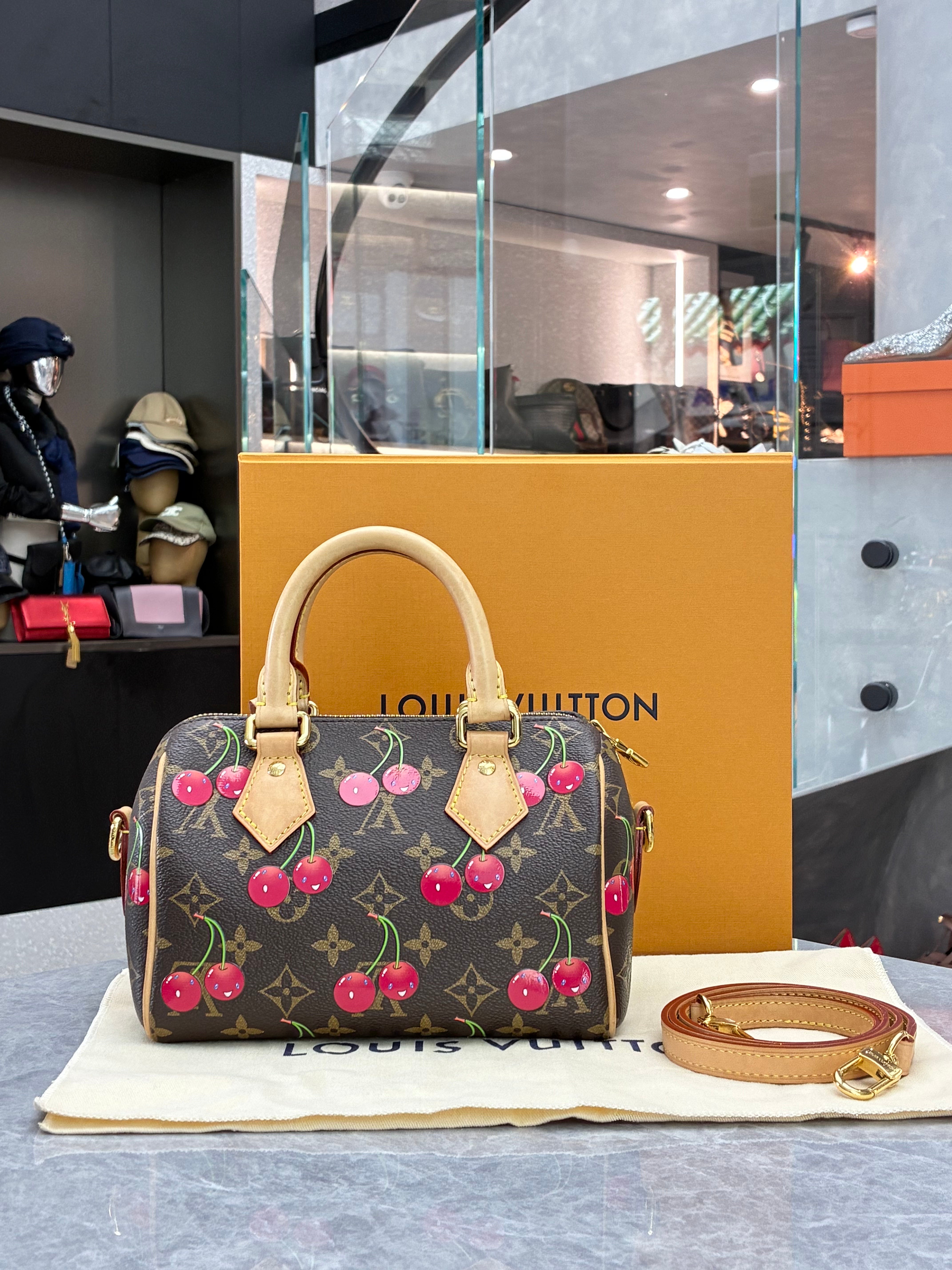 Louis Vuitton × Takashi Murakami Speedy Bandoulière 20 bag in monogram canvas features a playful cherry print and gold-tone hardware.